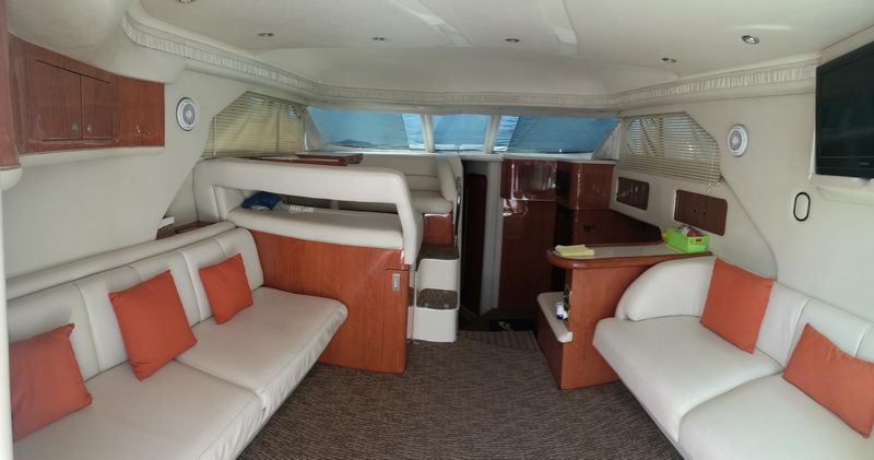 Main salon of 41 ft Sea Ray flybridge yacht with white leather sofas, orange cushions and wood cabinetry, Cancun luxury charter