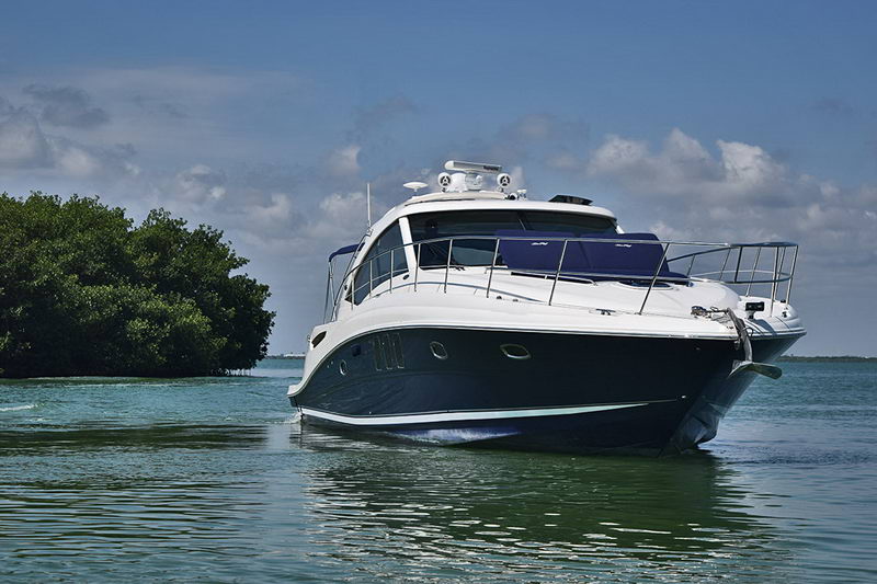 Bow-on front view of the navy-hulled Sea Ray cruiser on calm green water near a mangrove island, showing the raked bow, bow rail and radar arch. Clear sky with scattered clouds.