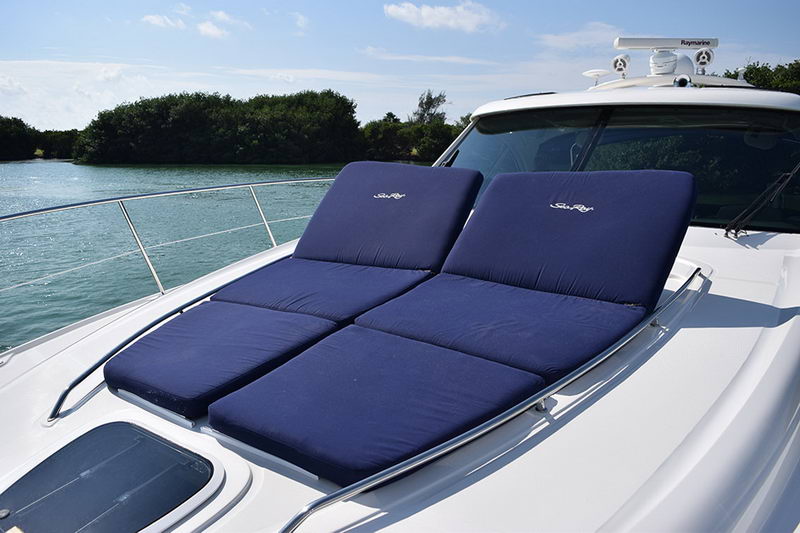 Foredeck of the Sea Ray with twin navy sunpad cushions bearing the Sea Ray logo, bordered by stainless rails, with a radar dome and the lagoon visible alongside.
