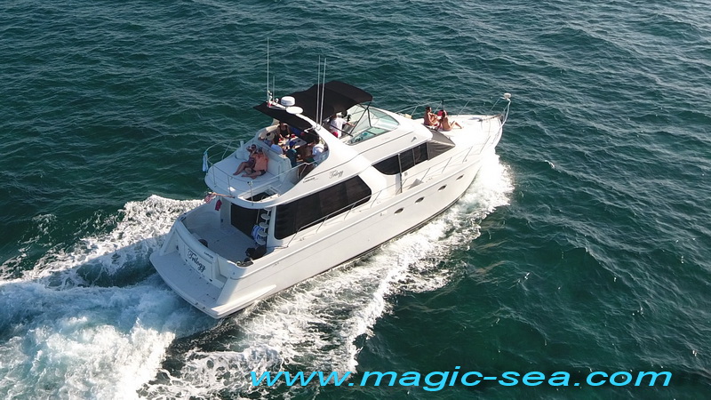 Aerial of a white motor yacht underway with people aboard, cutting through deep blue water; a 'www.magic-sea.com' watermark is overlaid across the bottom.