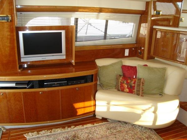 Salon interior with a cream leather sofa with red and green pillows, a glossy wood entertainment cabinet holding a Panasonic TV and electronics, a window with blinds and an oriental rug.