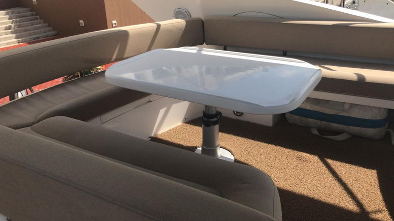 Aft deck seating area of Sunseeker 64 ft charter yacht at marina with grey banquette upholstery and white folding table