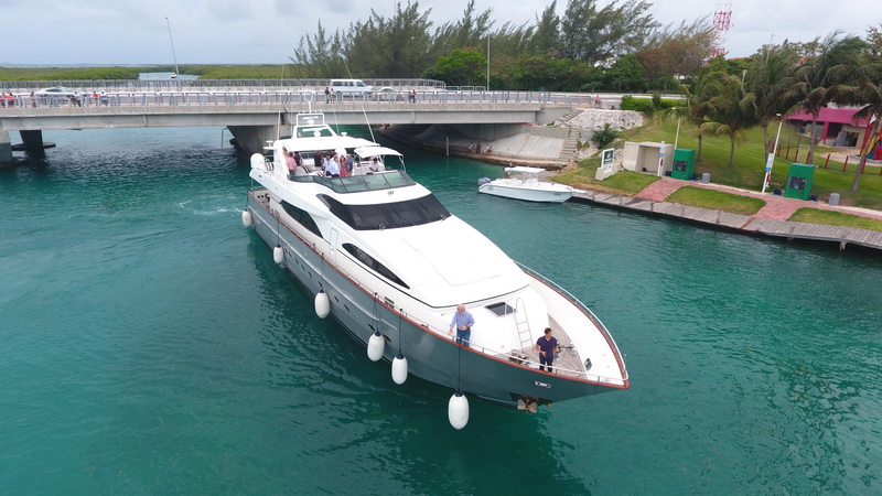 Aerial drone view of 100-foot Azimut mega yacht rental passing Cancun marina bridge with guests celebrating on flybridge