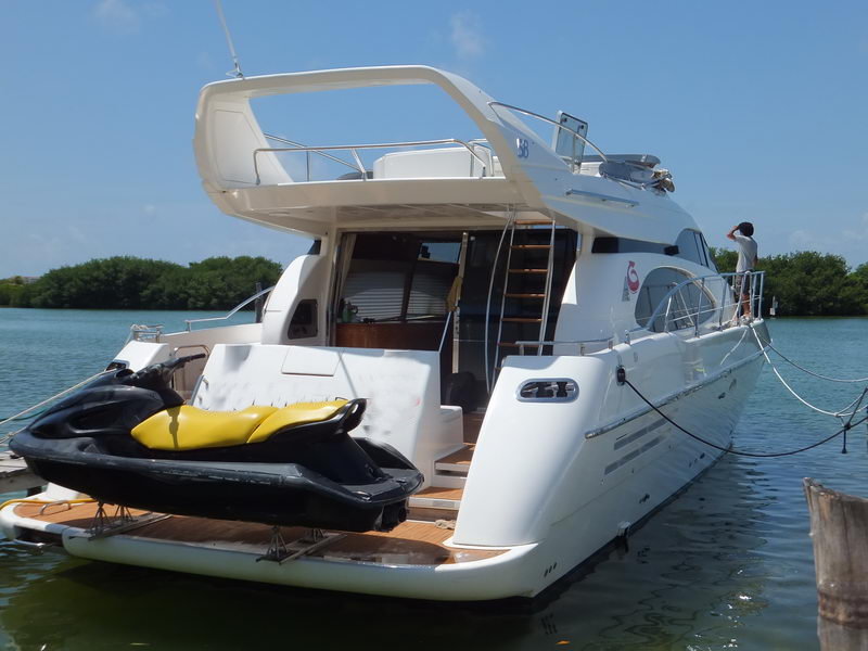 Aft view of Azimut 60 ft charter yacht at marina showing flybridge deck, boarding ladder and jet ski on swim platform