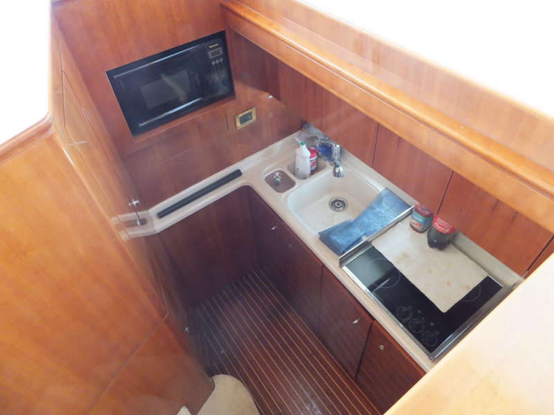 Compact galley kitchen of Azimut 60 ft yacht with microwave, sink, induction cooktop and mahogany cabinetry below deck