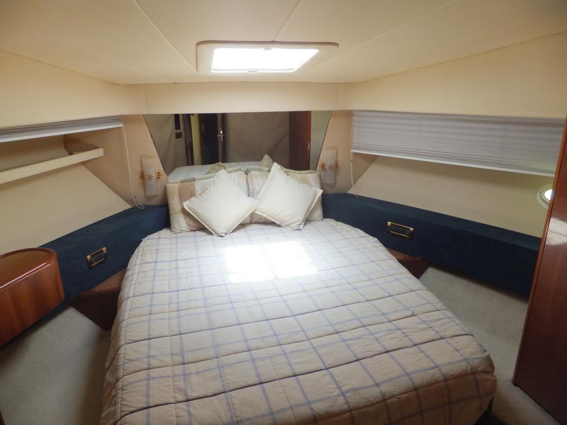 Forward stateroom of Azimut 60 ft luxury yacht with double bed, plaid bedding, porthole windows and wood night tables