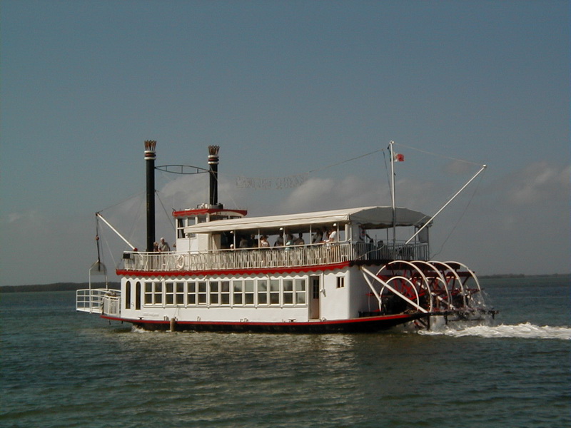Barco Cancun Queen con dos chimeneas y rueda de paletas roja navegando aguas turquesa de la laguna bajo cielo azul, Cancún