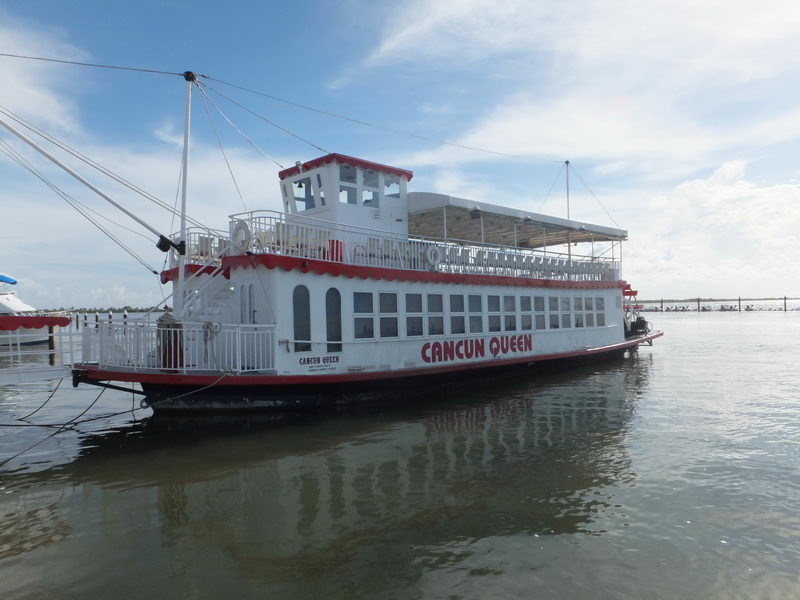 Barco de paletas Cancun Queen blanco y rojo atracado en la marina de la Laguna Nichupté bajo un cielo azul brillante de Cancún