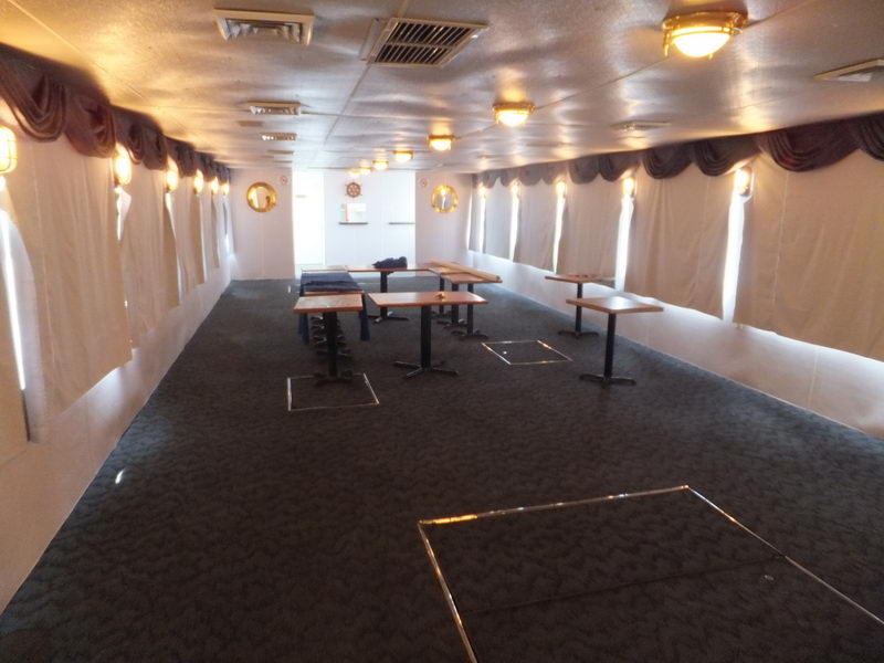 Amplio salón comedor interior del Cancun Queen con mesas de madera y ojos de buey con cortinas, listo para un evento privado