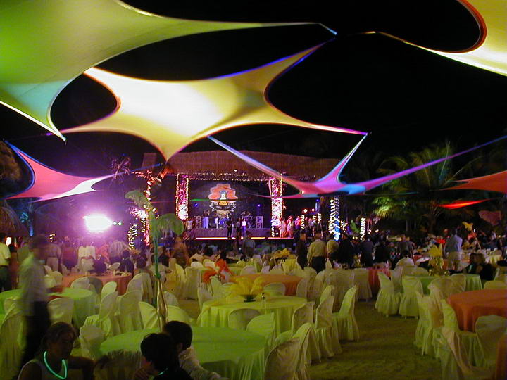 Colorful sail-canopy beach gala at night with stage, banquet tables and hundreds of seated guests at a Caribbean group event