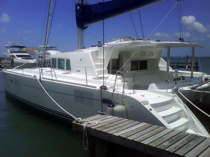 White Lagoon 440 catamaran moored at a dock, three-quarter bow-to view showing the topsides, coachroof windows, boarding steps and stainless rails, with another power yacht alongside under a bright sky.