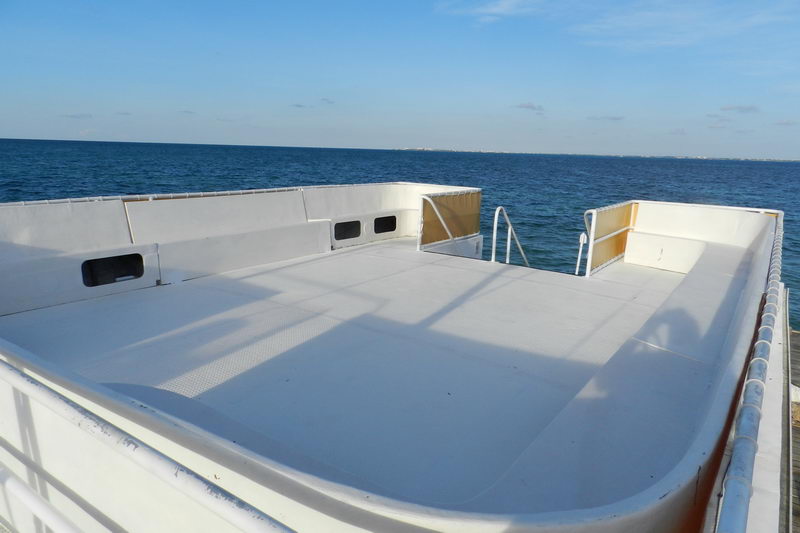 Empty white upper sun deck of the catamaran with a boarding ladder, shot toward open blue sea under a clear sky, sunny.