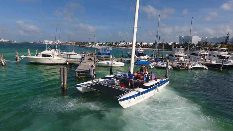 White-and-blue catamaran 'Double Eagle' moored in shallow turquoise water near a dock with a blue Bimini and a dinghy alongside, sunny.