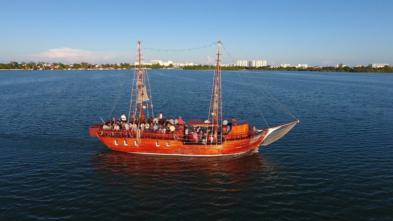 Stern view of the Columbus galleon full of guests on deck sailing the calm lagoon under a clear blue sky in Cancun
