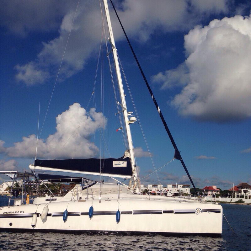 Side profile of the Lavezzi 42 catamaran in Cozumel showing tall mast and twin hulls under bright clouds