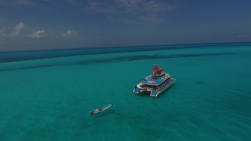 The Dancer catamaran moored over a shallow turquoise reef near Isla Mujeres with a small tender boat nearby under a bright sky