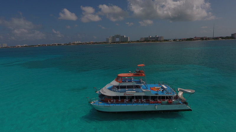 Aerial view of the three-deck Dancer party catamaran anchored over turquoise water with the Cancun hotel zone skyline behind