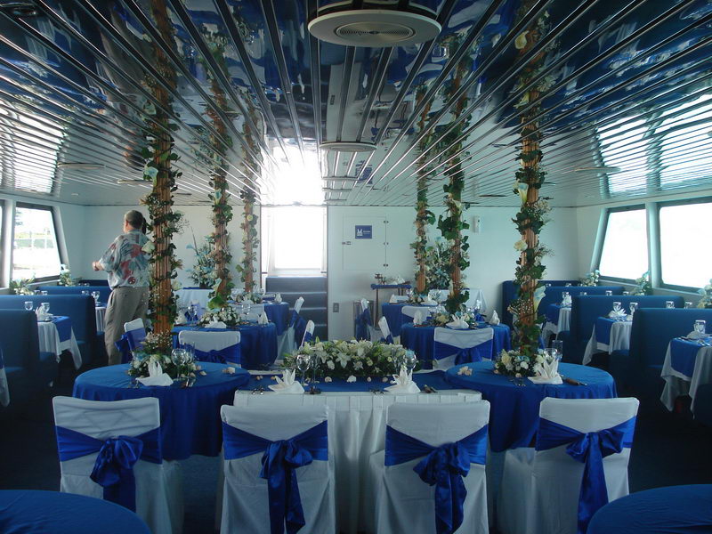 Symmetrical view of the Discovery's wedding reception with blue sashes, floral-wrapped columns and a head table facing the windows