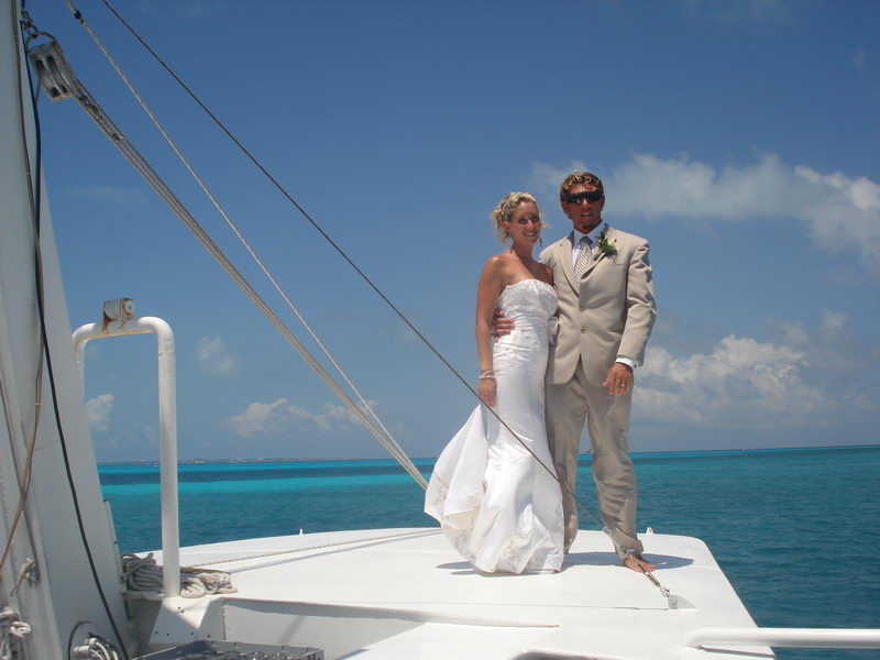 Bride in a white gown and groom in a beige suit posing on the bow of the Discovery boat above brilliant turquoise Caribbean water