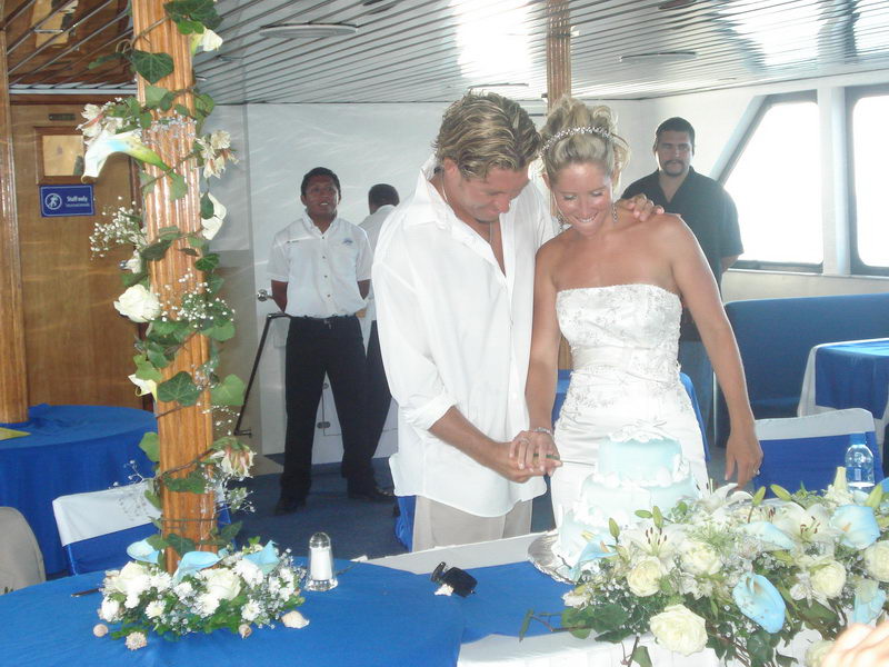 Bride and groom cutting a seafoam-blue seashell wedding cake in the Discovery's blue-and-white decorated salon