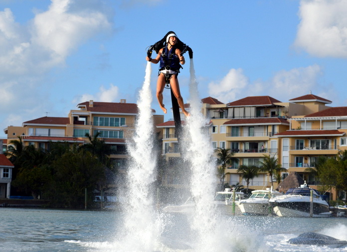 Persona impulsada por un jetpack de agua muy por encima de una marina de Cancún con condominios frente al mar y yates detrás