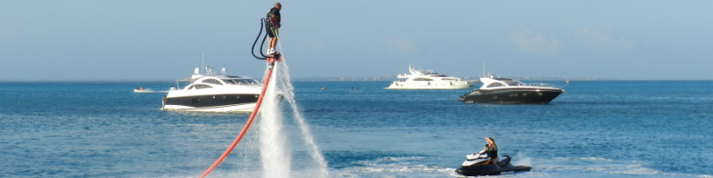 Flyboarder hovering on a jet of water above the turquoise Cancun bay with luxury yachts and a jet ski in the background
