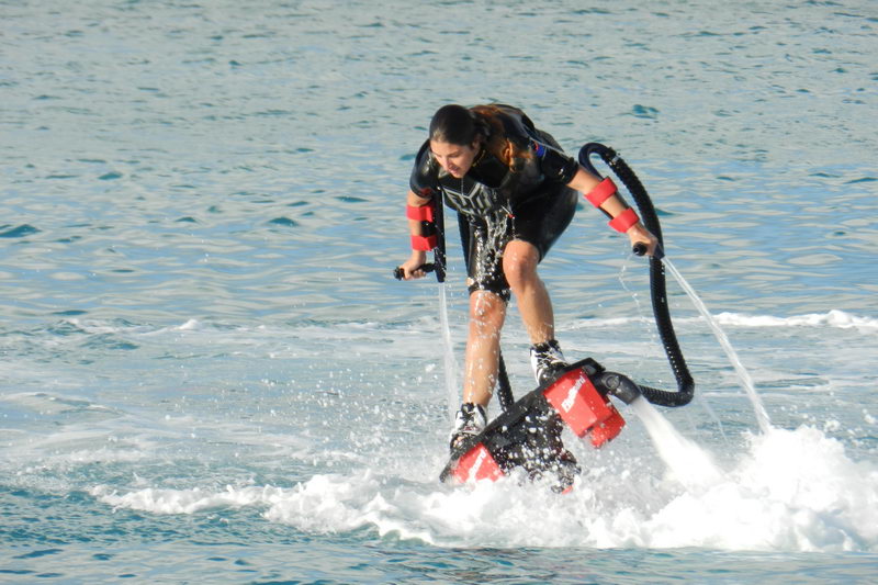 Primer plano de un rider de flyboard inclinado sobre el agua con chorros saliendo de la tabla, deporte acuático extremo en Cancún