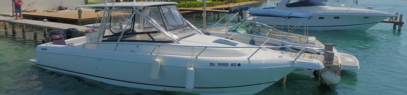 White Intrepid 32 sport fishing boat with hardtop moored at a Cancun marina dock beside larger yachts on calm turquoise water