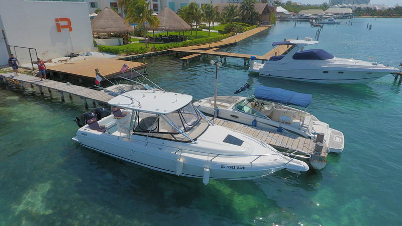 fishing boat docked beside a pier and other yachts on clear turquoise Cancun water