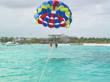 Parasailer floating under a colorful canopy high above the turquoise Cancun bay towed by a boat