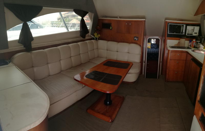 Salón del yate de pesca Luhrs de 38 pies con sofá de piel color crema, mesa de madera y cocina, charter en Puerto Aventuras