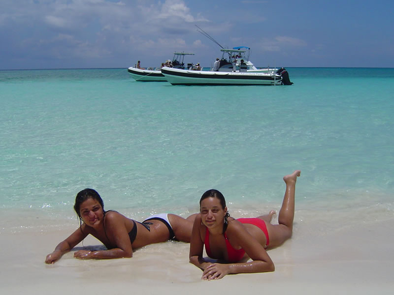 Two guests relaxing on pristine white sand Caribbean beach with F1 Zodiac speedboat anchored offshore on Riviera Maya private charter
