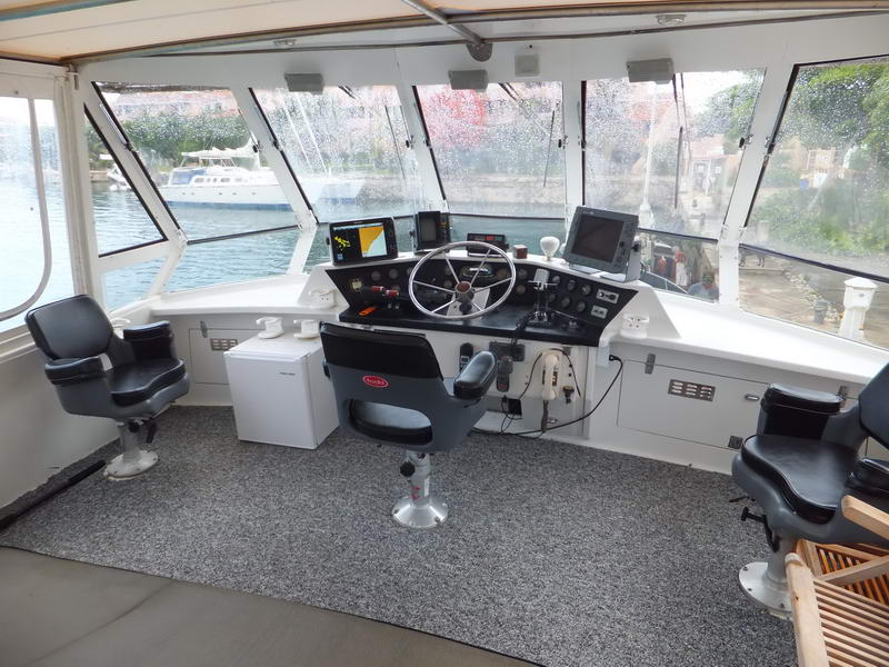 Flybridge helm station with large steering wheel, navigation electronics and three black helm chairs