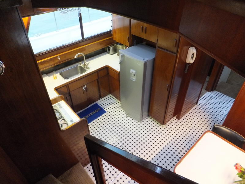 Yacht galley with stainless sink, tall refrigerator and wood cabinetry — where the fire-grilled chicken lunch is prepared