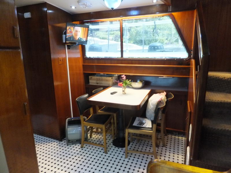 Dining nook with white-topped table, dark upholstered chairs and a wall-mounted TV for karaoke