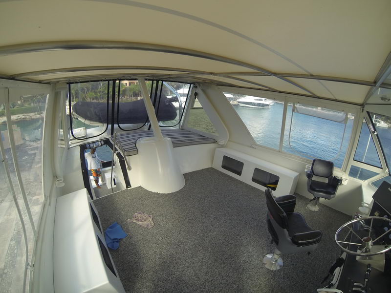 Enclosed flybridge with grey carpet, black helm chairs, steering wheel and bench seating