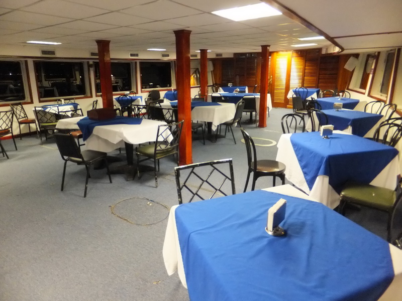Evening salon of the Princess boat with blue-topped tables and chairs arranged for a group dinner along the windows