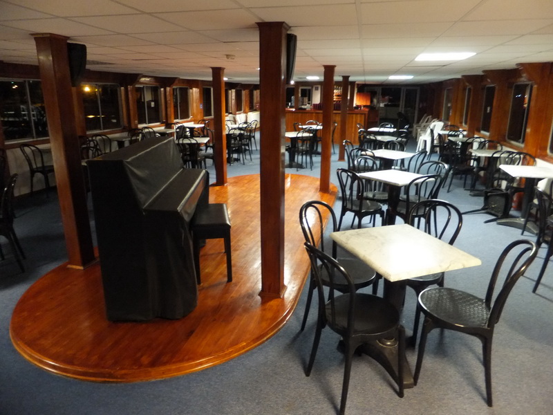 Interior deck of the Princess boat with a parquet dance floor and stage piano surrounded by bistro tables and a wood bar