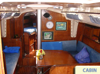 Salón interior con paneles de madera, mesa de comedor y literas azules a bordo del velero de 40 pies, charter privado Cancún