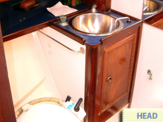 Baño compacto con lavabo de acero inoxidable y mueble de madera a bordo del velero de 40 pies, amenidad charter Cancún