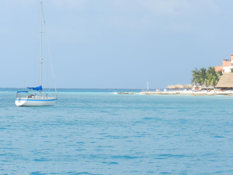 Velero fondeado en aguas turquesas frente a la playa con palapas de Isla Mujeres, ideal para paseos en velero desde Cancún