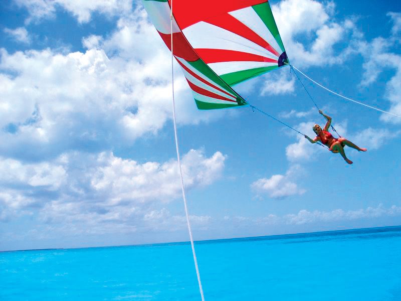 Woman parasailing over vivid turquoise Caribbean Sea near Isla Mujeres, optional water sport activity on Cancun catamaran day tour