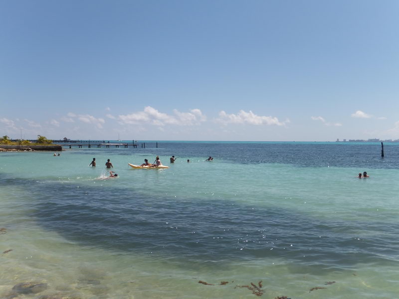 Guests swimming and kayaking in shallow turquoise Caribbean water at the Isla Mujeres beach stop on the Samba catamaran day tour