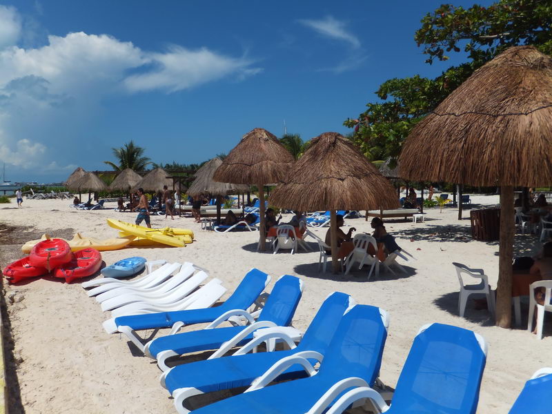 Lounge chairs, kayaks and thatched palapas at the Isla Mujeres beach club included in the Samba catamaran day tour from Cancun