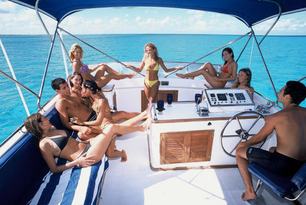 Group of friends relaxing on the Sandralyn's flybridge helm station over bright turquoise Caribbean water near Isla Mujeres