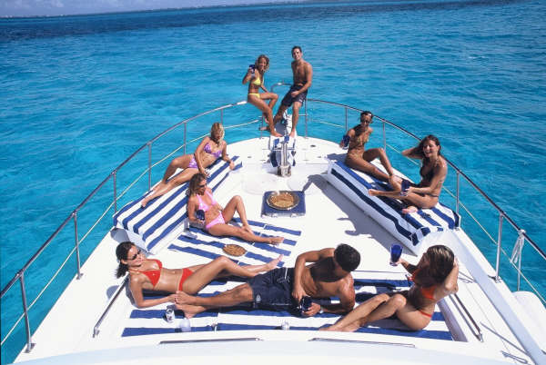 Friends lounging on the Sandralyn's striped bow sun pads with snacks over vivid turquoise water near Isla Mujeres, Cancun