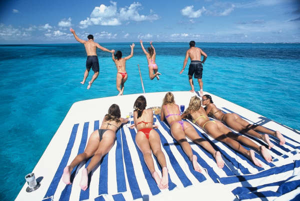 Guests sunbathing on striped towels and leaping off the Sandralyn's stern into clear turquoise Caribbean water