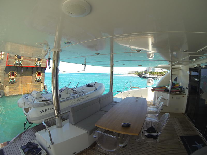 Aft deck lounge and dining table of the 66 ft Sunreef catamaran with tender alongside in turquoise Caribbean water, Cancun charter