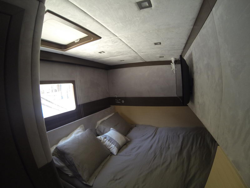 Cozy guest cabin with double bed, hull window and TV aboard the 66 ft Sunreef catamaran, luxury yacht charter Cancun