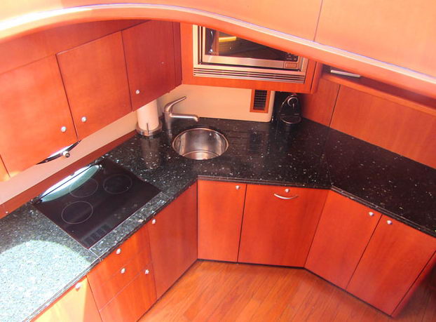 Overhead view of a yacht galley with cherry-wood cabinetry, black granite countertops, a stainless sink, built-in stovetop, and a microwave mounted above the counter.